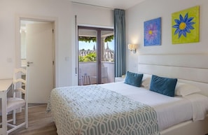 Habitación de hotel con cama, escritorio, silla y balcón con vistas.
