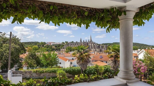 Un balcon offrant une vue sur une cathédrale historique, une végétation luxuriante et une colonne de pierre.