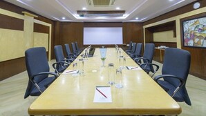 A conference room with a long table, chairs, a projector screen, and a painting on the wall. - The Fern Residency Yeshwanthpur (Bengaluru)