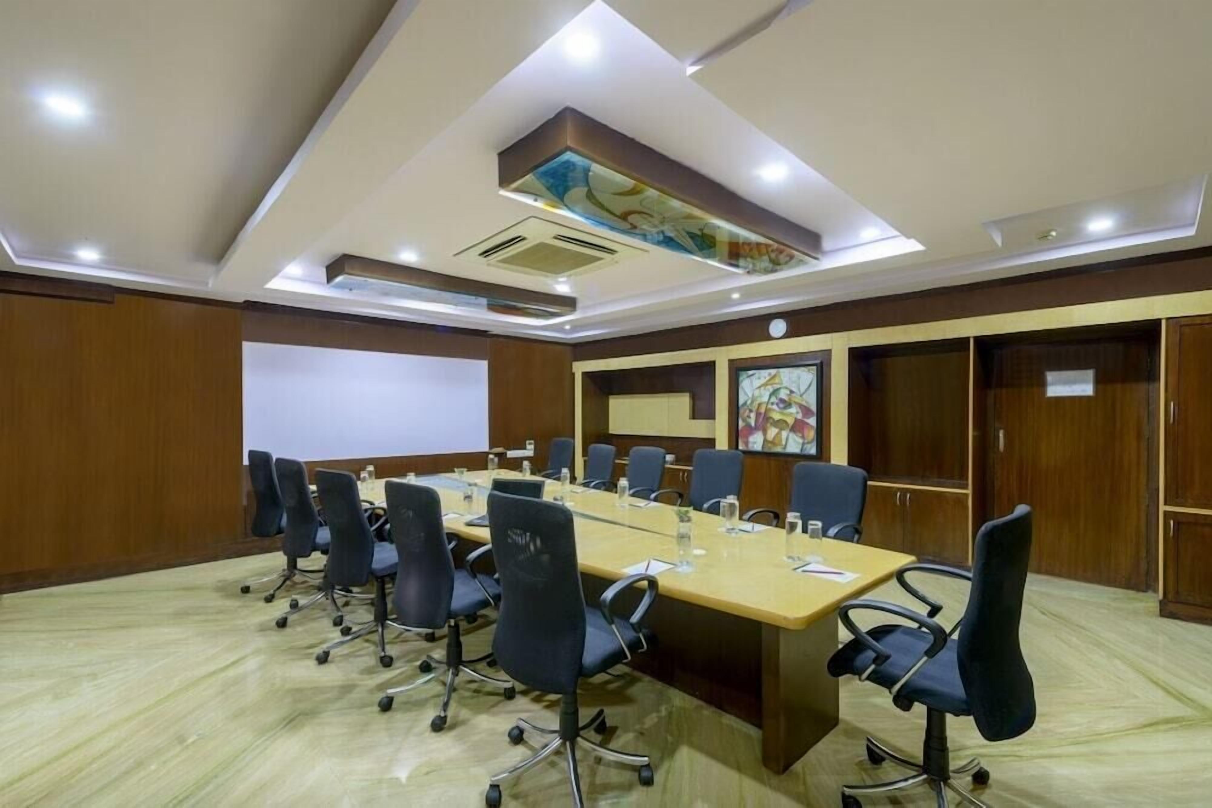 A conference room with a long table, multiple chairs, and a projector screen.