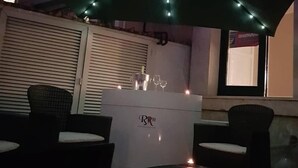 Ein Sitzbereich im Freien mit Korbstühlen und einem Tisch, beschattet von einem grünen Sonnenschirm.