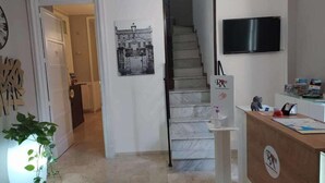 Ein Hotel-Empfangsbereich mit Treppe, Empfangstresen, Wand-Fernseher und einem gerahmten Bild an der Wand.