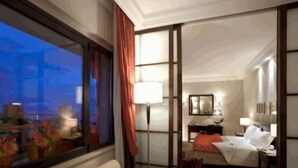 Ein Hotelzimmer mit großem Fenster, einem Bett, einem Schreibtisch und einem Sessel.