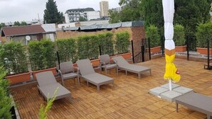 Une terrasse sur le toit, avec des chaises longues, un parasol jaune et des plantes en pot.