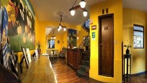 A hotel lobby with a wooden reception desk, a mural on the wall, a staircase, and a yellow wall. - Sierra Madre (Quito)