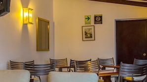 Un comedor con sillas y mesas de madera, una lámpara fijada a la pared y una puerta con un letrero que indica una salida.