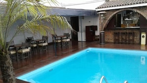 Una piscina con zona de bar, sillas y una palmera.