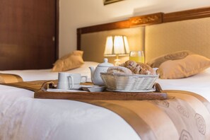 A neatly made breakfast tray with bread, a teapot, cups, and a glass of orange juice on a bed with a headboard and pillows. - El Doral Aparthotel (Lima)