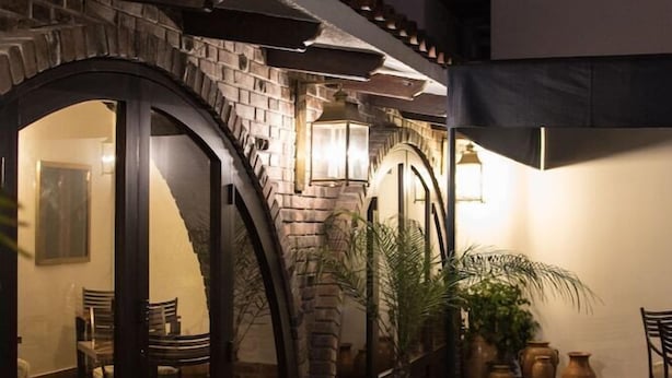 Un patio techado al aire libre con pared de ladrillo, puerta de vidrio que da al interior y plantas en macetas.