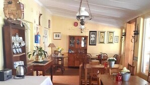 Un comedor con mesas y sillas de madera, una araña y una estantería con diversos objetos.