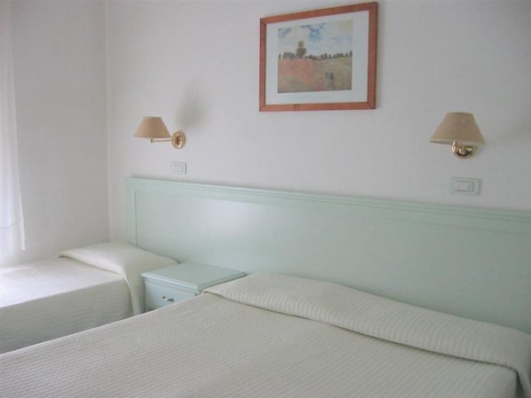 A hotel room with two single beds, a light blue headboard, two bedside lamps, and a framed painting on the wall.