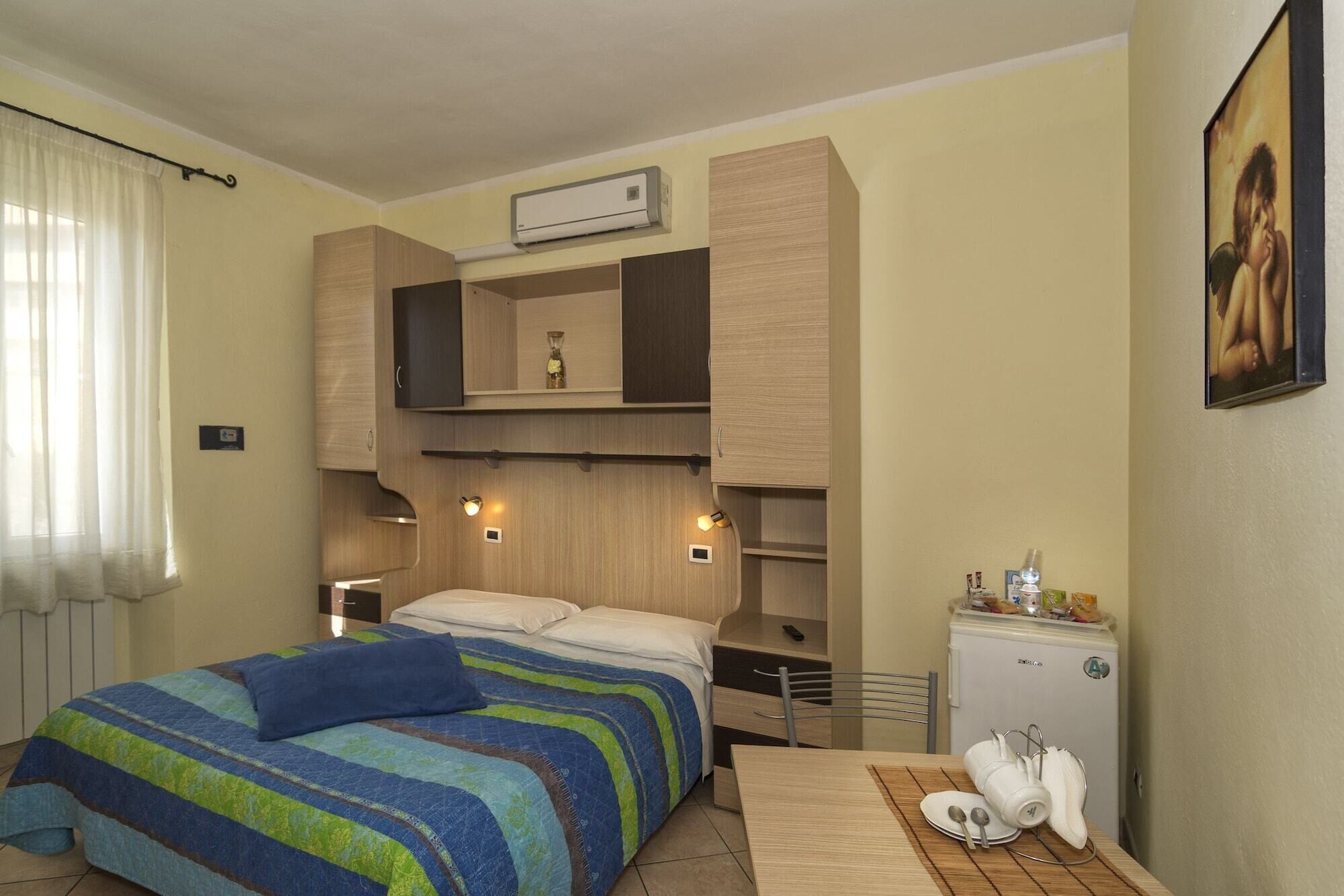A bedroom with a bed, built-in shelves, a small refrigerator, and a painting on the wall.