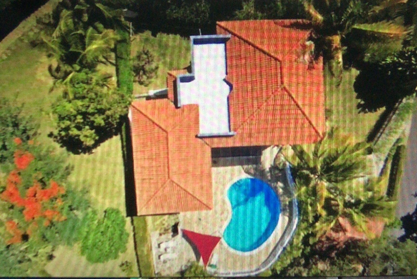 Vista aérea de una propiedad con piscina, una casa grande con techo rojo y vegetación circundante.