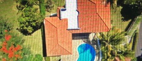 Vista aérea de una propiedad con piscina, una casa grande con techo rojo y vegetación circundante.