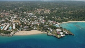 An aerial view of a coastal town with a beach, clear blue waters, and a mix of residential and commercial buildings. - Pool Jacuzzi & Tropical Oasis Yard With Fruit Trees (Sosua)