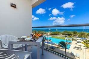 A balcony with a table set for breakfast, overlooking a pool and beach area.