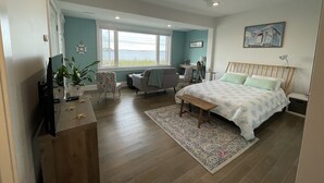 A bedroom with a bed, a desk, a chair, a TV, and a window with a view. - The Blue Pearl (Nahant)
