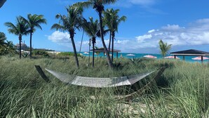 A hammock in a grassy area with palm trees and a beach in the background. - Grace Bay Prime Location 2 Bedroom Condo with Beach, Pool and Tennis access!! (Grace Bay)