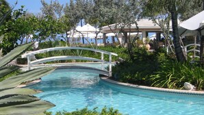 A pool with a white bridge, surrounded by lush greenery and palm trees. - Grace Bay Prime Location 2 Bedroom Condo with Beach, Pool and Tennis access!! (Grace Bay)