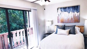 Une chambre avec un grand lit, un ventilateur de plafond, un tableau et une vue sur la verdure grâce à une porte coulissante.