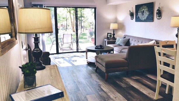 Un salon avec un canapé, une table basse et une lampe. On y trouve une table en bois sur laquelle sont posés une plante et un dossier. Une chaise est visible dans un coin.