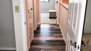 Un couloir étroit, doté d’un plancher en bois et d’escaliers recouverts de moquette, mène à une pièce avec une fenêtre et un banc.