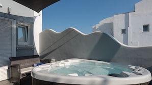 A hot tub on a patio with a wicker chair and a small table. - Oasis Hotel Fira (Santorini)