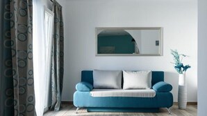 A modern living room with a blue sofa, a large mirror, and a potted plant. - Oasis Hotel Fira (Santorini)