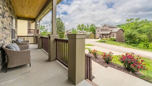 A covered porch with wicker furniture, a stone wall, and a view of a residential street with houses and greenery. - Family Style 6 Bedroom Home, 2 Pools, New Patio Furniture!  Clean & Relaxing! (Hollister)