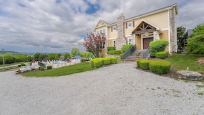 A two-story house with a stone chimney, a front porch, and a gravel driveway. - Family Style 6 Bedroom Home, 2 Pools, New Patio Furniture!  Clean & Relaxing! (Hollister)
