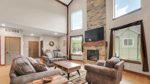 A spacious living room with a fireplace, two sofas, a coffee table, and a TV mounted on the wall. - Family Style 6 Bedroom Home, 2 Pools, New Patio Furniture!  Clean & Relaxing! (Hollister)