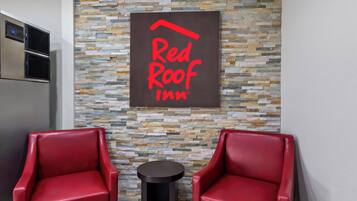 A Red Roof Inn sign on a textured stone wall, two red leather chairs, and a small round table.