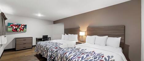 A hotel room with two beds, a desk, a chair, a lamp, and a painting on the wall.