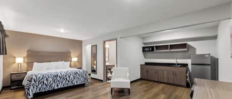 Une chambre d’hôtel moderne équipée d’un grand lit, d’un petit bureau, d’une chaise, d’une kitchenette et d’une salle de bain.