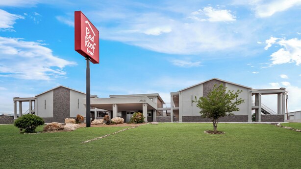 A modern building with a sign for Red Roof Inn, featuring a covered entrance and a well-maintained lawn.