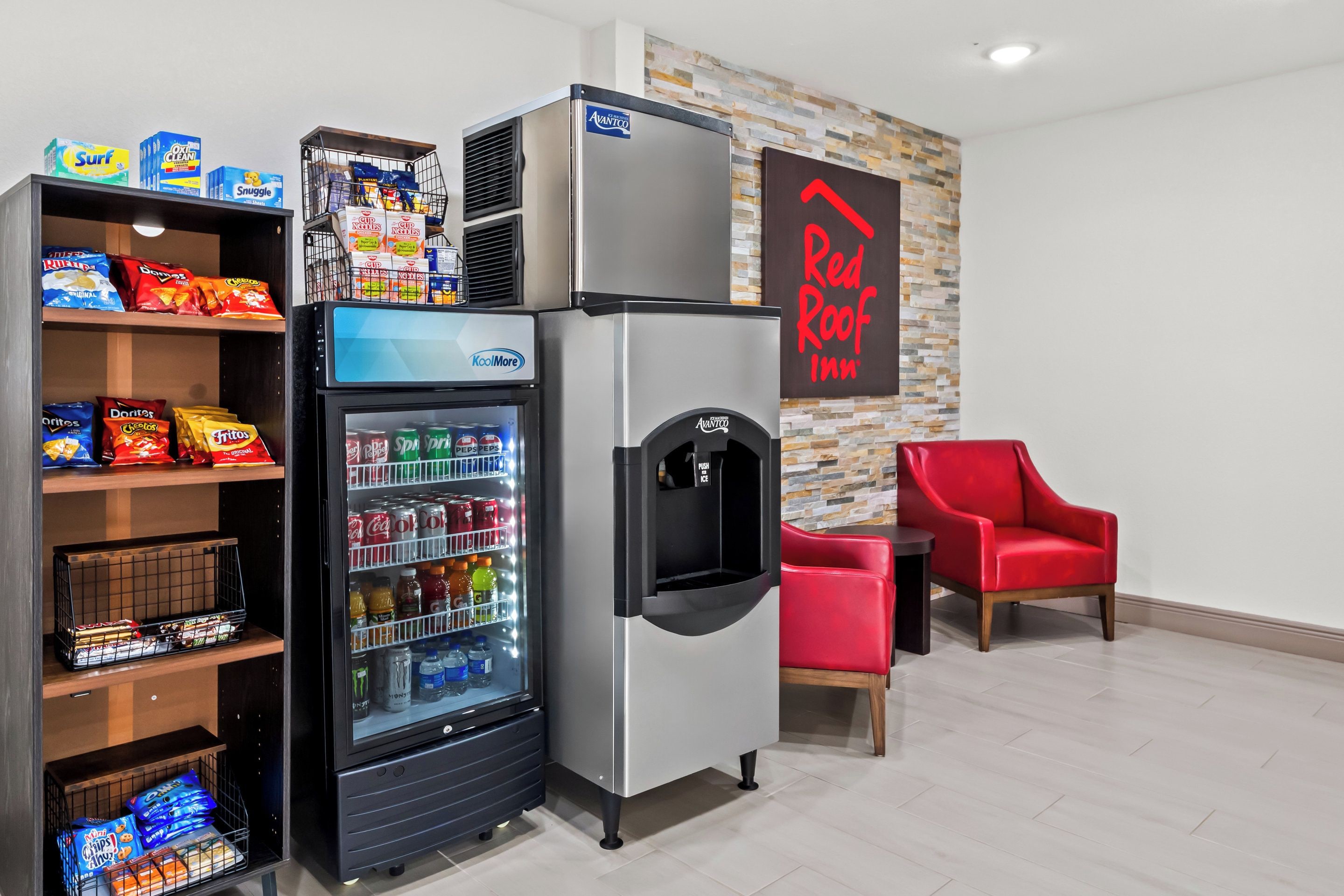 Una máquina expendedora de aperitivos, un refrigerador y una silla roja en una habitación de hotel.