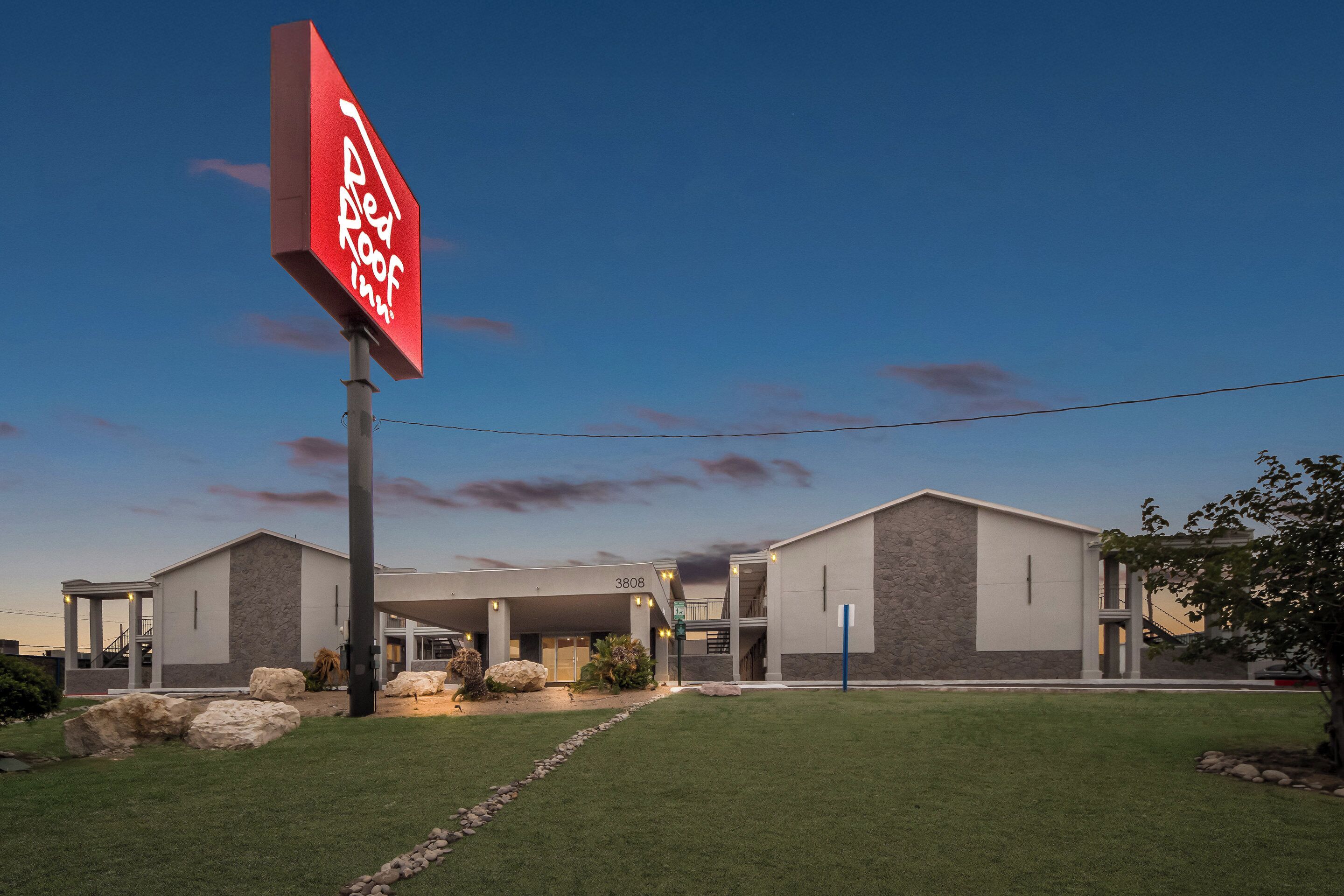 A modern building with a large sign reading "Red Roof Inn." It features a covered entrance, a stone facade, and a well-maintained lawn.