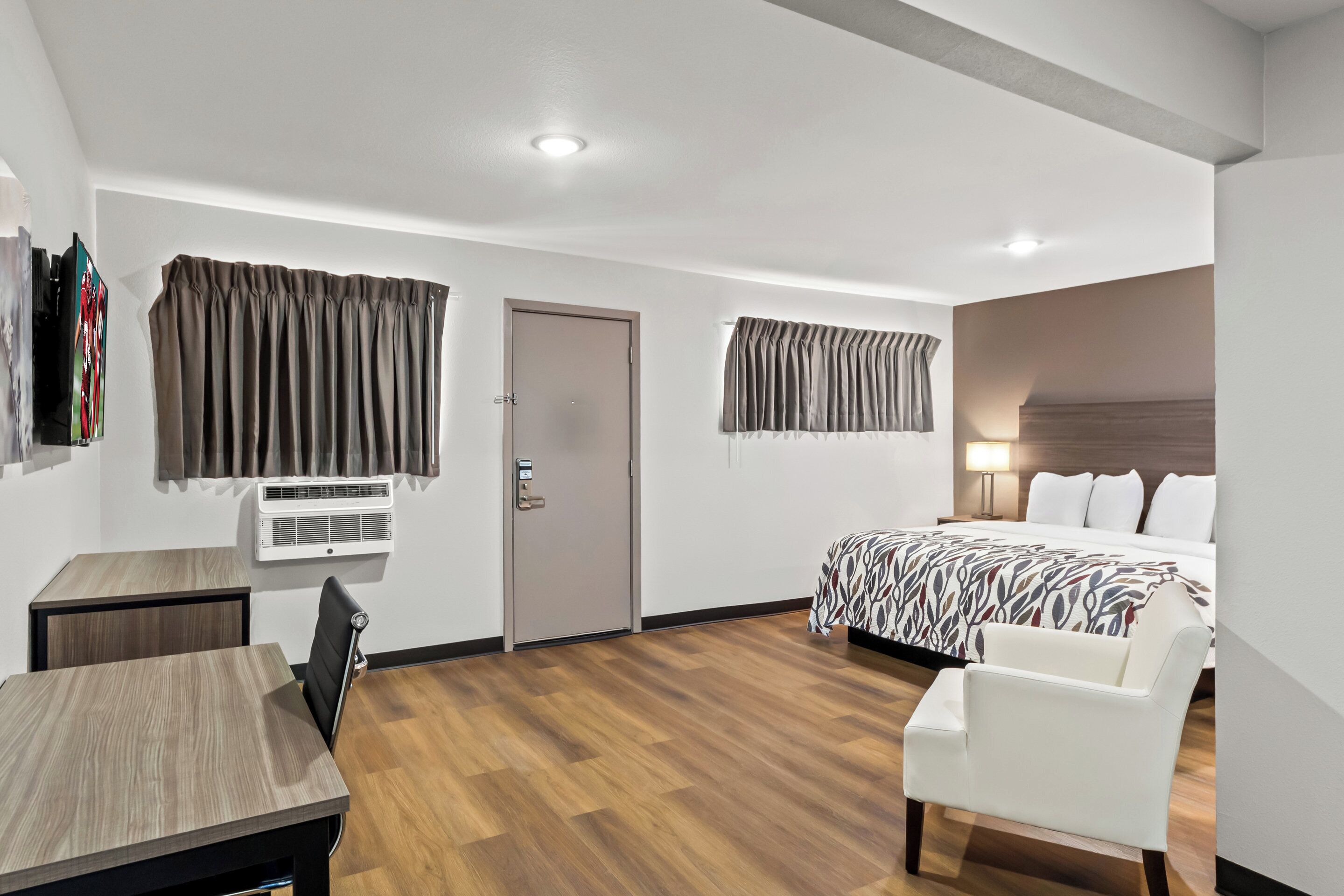 A hotel room with a bed, a desk, a chair, a wardrobe, and a window with curtains.