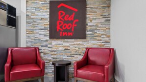 Two red leather armchairs and a small round table in a room with a stone wall and a Red Roof Inn sign. - Red Roof Inn Del Rio (Del Rio)