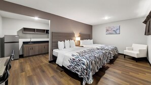A modern hotel room with a bed, bedside table, lamp, and a small seating area. - Red Roof Inn Del Rio (Del Rio)