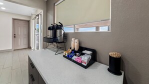 A kitchen area with a countertop displaying various items, a window with a blind, and a door leading to another room. - Red Roof Inn Del Rio (Del Rio)