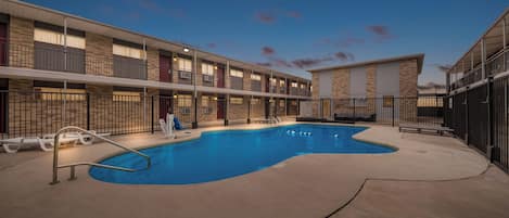 Un hotel con piscina, zona de estar al aire libre y un edificio de varios pisos con balcones.