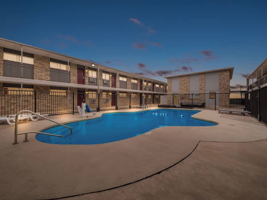 Un hotel con piscina, zona de estar al aire libre y un edificio de varios pisos con balcones.