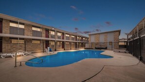 A hotel with a swimming pool, outdoor seating, and a multi-story building with balconies.