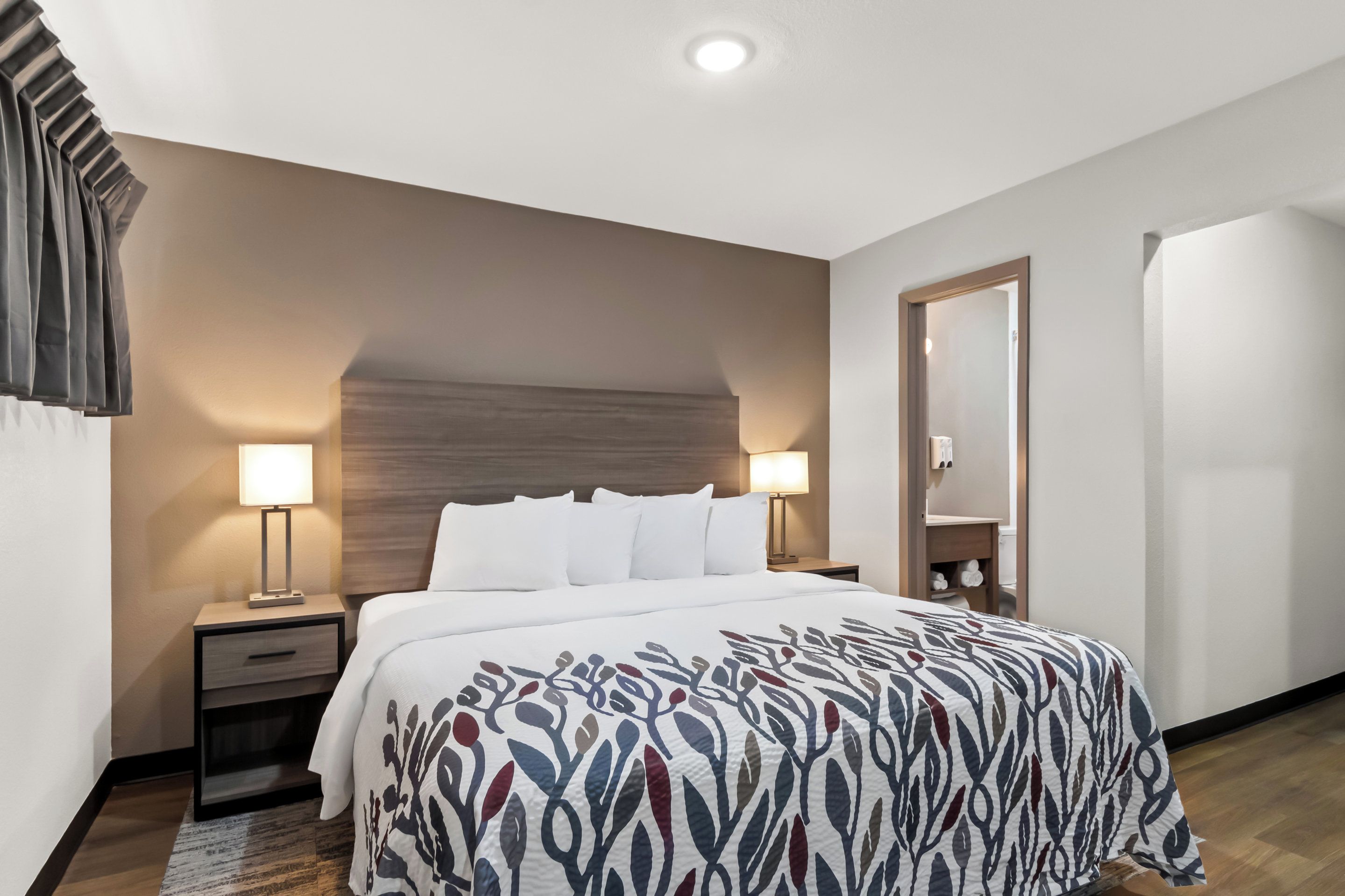 A hotel room with a large bed, two bedside tables, a nightstand, a wooden headboard, and a mirror.