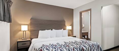 A hotel room with a large bed, two bedside tables, a nightstand, a wooden headboard, and a mirror.