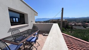 Un balcón con mesa y sillas, con vistas a un paisaje que incluye una masa de agua y montañas a lo lejos.