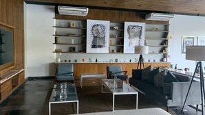 A modern living room with a sofa, chairs, a coffee table, and a bookshelf with framed artwork. - Exclusive apartment in Residencial Vía Montejo (merida)