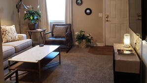 A living room with a sofa, a coffee table, a chair, a lamp, a potted plant, a television, and a door.
