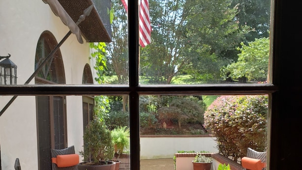 A patio with two wicker chairs and a small table, surrounded by potted plants and a brick floor.